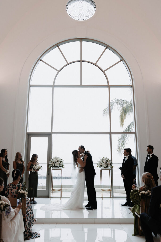 indoor ceremony couple kissing in front of large ocean facing window