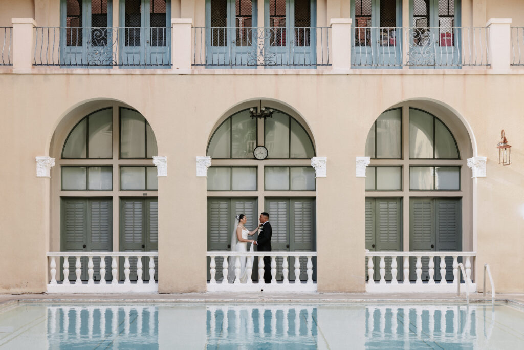 Bride and groom sharing a romantic moment beneath the elegant arches of Cafe Julia, showcasing the venue's timeless architecture and storytelling in wedding photography.