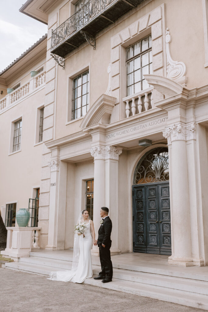 legant front view of Cafe Julia’s historic Mediterranean Revival architecture, showcasing its grand arches and timeless charm with couple holding hands, as a premier wedding venue.