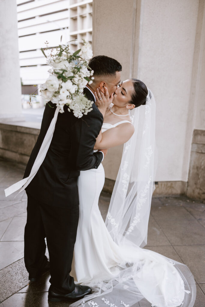 Bride and groom sharing a romantic kiss in the courtyard of Cafe Julia, surrounded by unique buildings and timeless architecture.