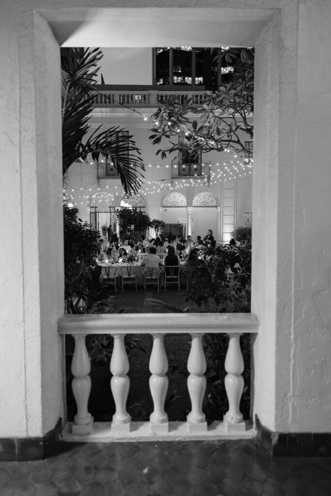 Nighttime view through a column at Cafe Julia, capturing guests mingling around beautifully lit reception tables under string lights, creating a warm and intimate atmosphere.