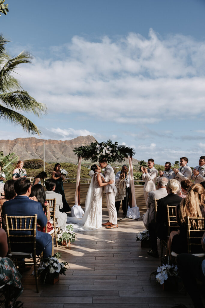 Couple first kiss at ceremony in front of Diamond Head at The Deck Waikiki