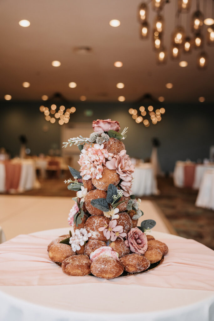 A tower of malasada donuts decorated with pink flowers and greenery displayed on a table at a wedding reception in The Queen Kapiolani Hotel in Waikiki, Honolulu.